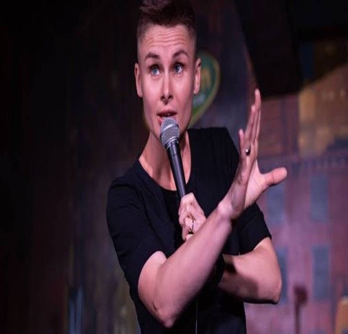 Comedian Ashley Gutermuth performing onstage with a microphone