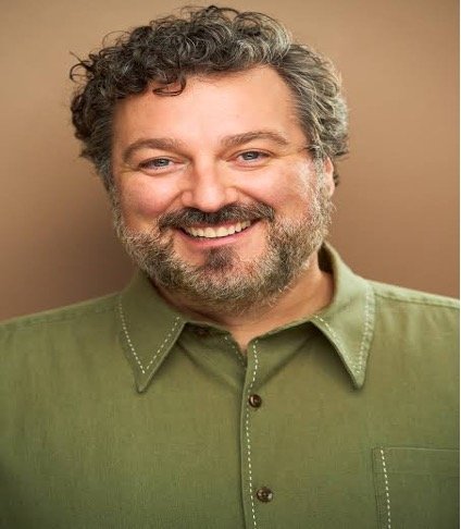 Comedian Mark Riccadonna smiling in a green shirt