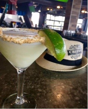 Key lime martini garnished with a lime wedge beside a straw hat