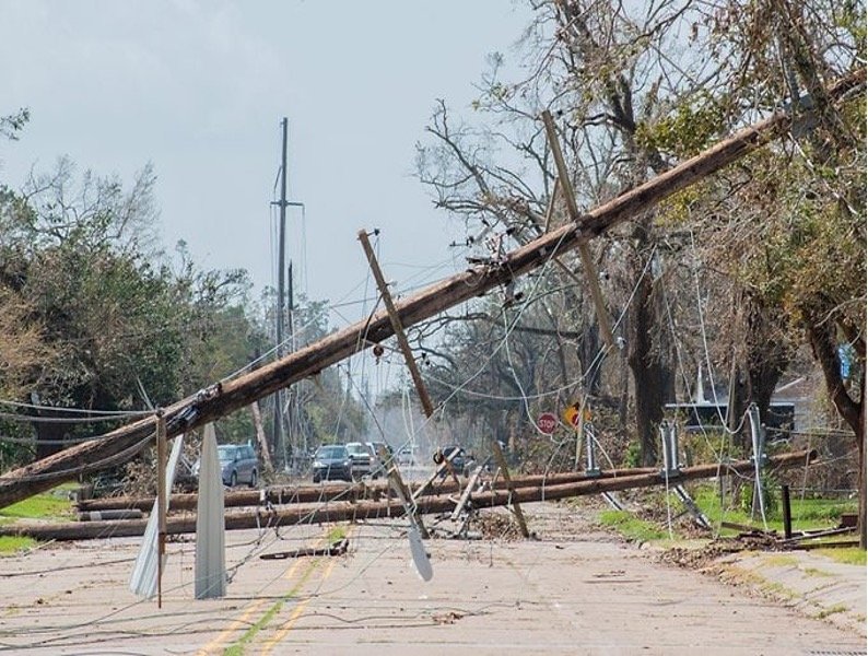 Snapped utility poles and downed power lines across a road after a hurricane